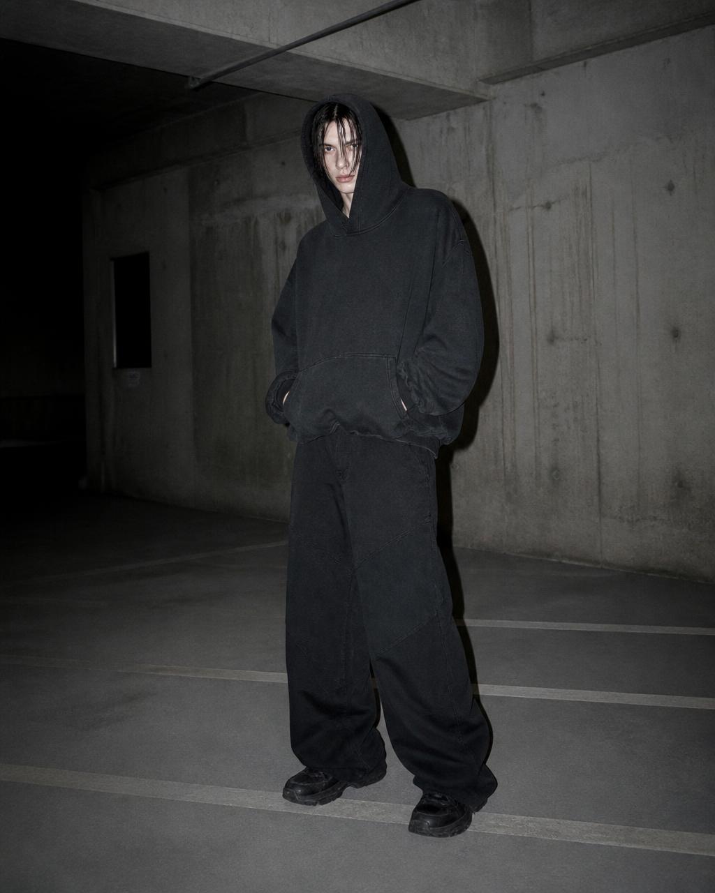 Model mengenakan hoodie berat oversized di basement parkir beton
