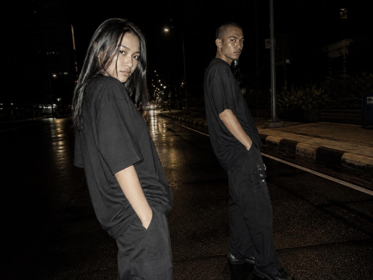 Dua model mengenakan kaos boxy hitam dan celana cargo di jalanan basah malam hari
